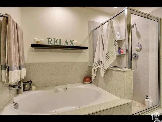 Soaking tub with a tiled surround, complemented by a glass-enclosed shower featuring a built-in shelf and chrome fixtures