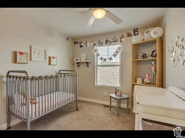 Carpeted room featuring a ceiling fan with integrated lighting, a window with blinds, and a built-in wooden shelving unit