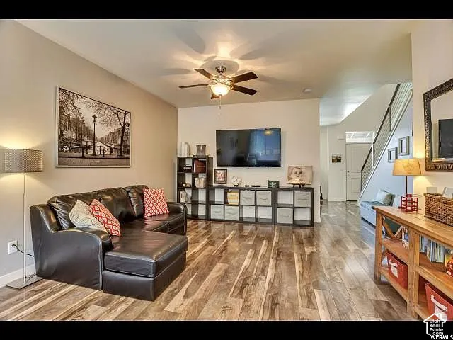 Spacious living area featuring wood-finish flooring, a ceiling fan with integrated lighting, and a wall-mounted television