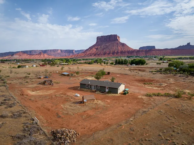 Expansive desert landscape featuring a single-story residence with a green exterior, set against a dramatic backdrop of red rock formations
