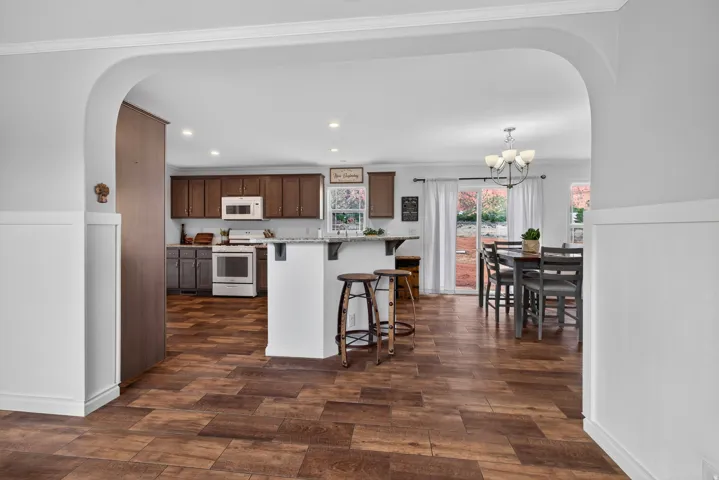 Open-concept living space featuring wood-finish flooring, an arched entryway, and white wainscoting