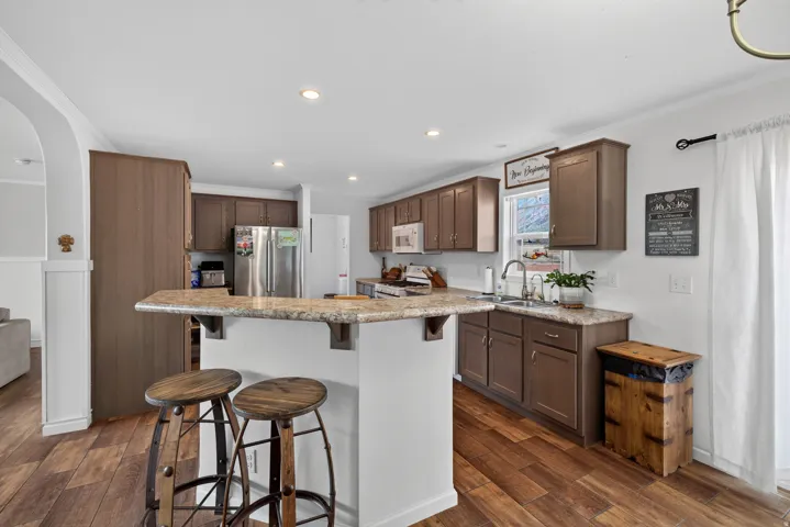 Kitchen featuring wood-finish flooring, recessed lighting, a breakfast bar, stainless steel appliances, and brown cabinetry