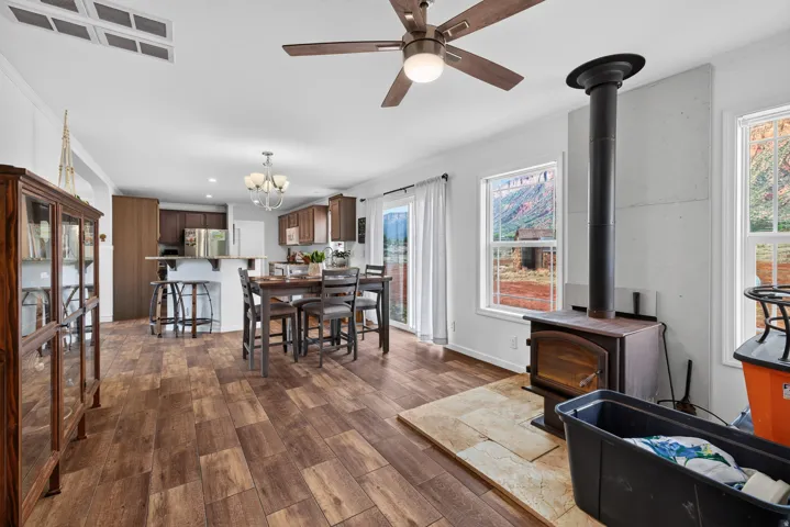 Spacious open-concept living area featuring wood-finish flooring, a contemporary ceiling fan, and a built-in wood-burning stove with a stone hearth