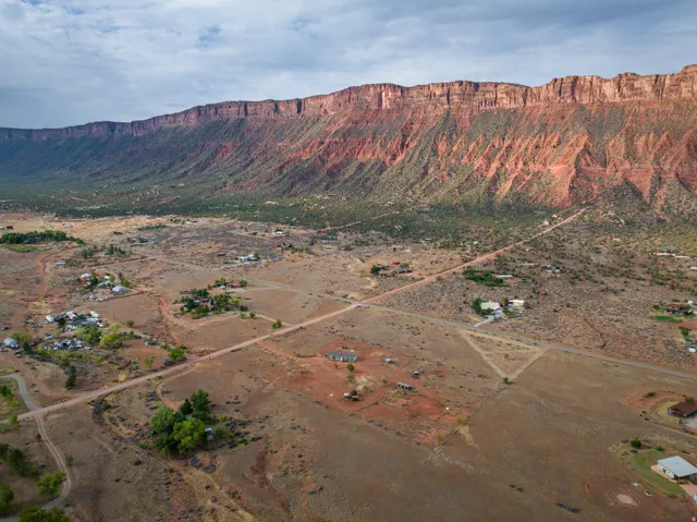 Expansive desert landscape featuring distant red rock formations, scattered natural vegetation, and unpaved roads