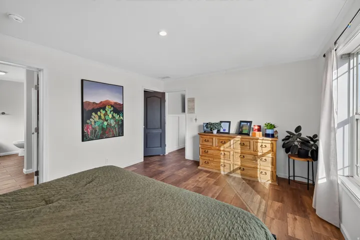 Spacious room featuring wood-finish flooring, white walls, and a large window with natural light