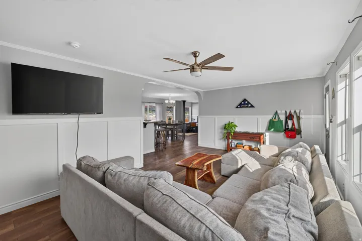Living area featuring wood-finish flooring, white wainscoting, and a ceiling fan with light fixture