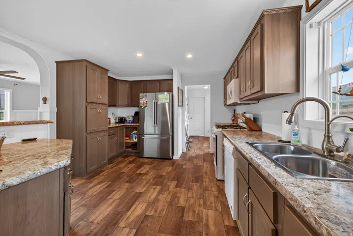 Spacious kitchen featuring wood-finish flooring, ample cabinetry, granite-style countertops, and a dual-basin stainless steel sink with a high-arch faucet