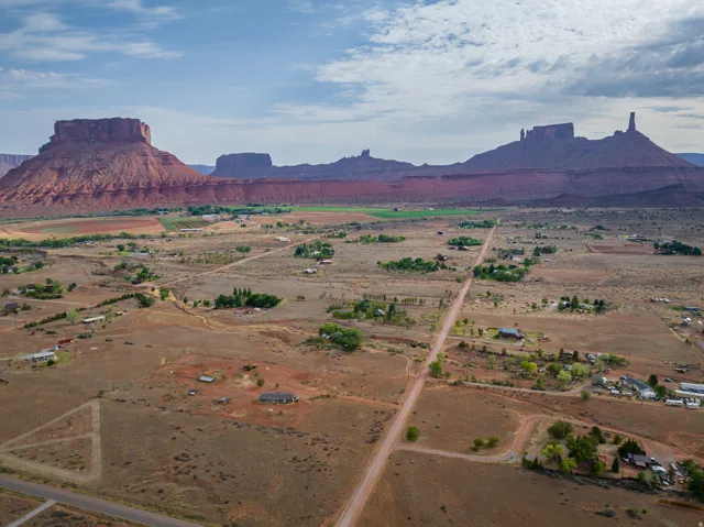 Expansive rural landscape featuring a network of unpaved roads and scattered residential properties, all set against a backdrop of towering red rock formations