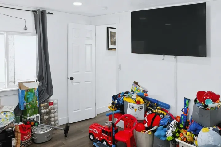 Recessed lighting illuminates this room featuring wood-finish flooring, a white paneled door with black hardware, and a window with a dark curtain rod