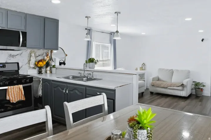 Kitchen featuring dark grey lower cabinetry, light grey upper cabinetry, an integrated double basin sink, and a black range with an overhead microwave