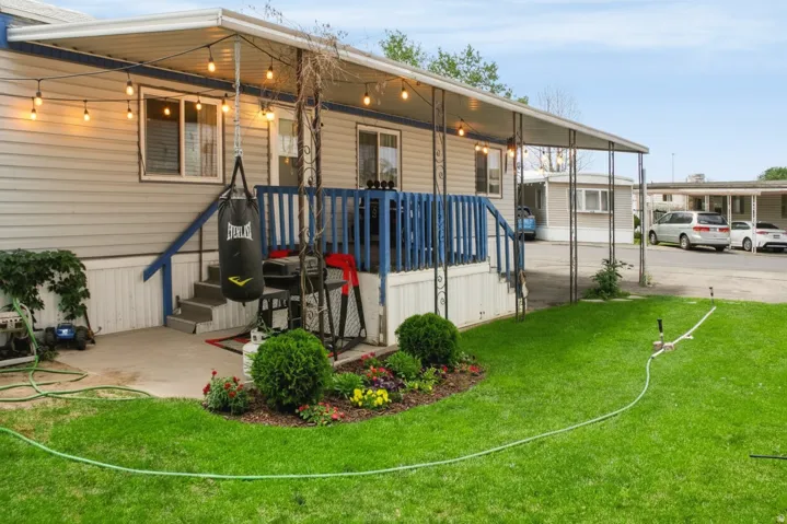 Covered outdoor patio area featuring string lighting, concrete steps with blue handrails, and a dedicated landscaped garden bed