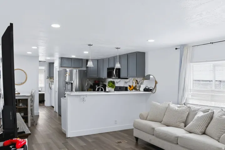 Open-concept living area featuring wood-finish flooring, recessed lighting, and a kitchen with gray cabinetry, stainless steel appliances, and a white countertop with a matching backsplash