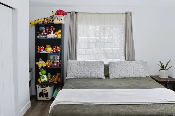 Room featuring a window with sheer and blackout curtains, wood-finish flooring, and a white wall finish