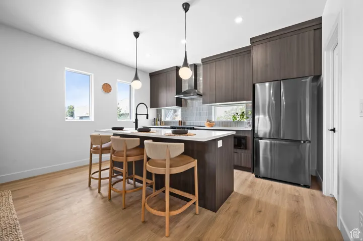 Kitchen featuring an island with seating, dark wood-finish cabinetry, a stainless steel refrigerator, and wood-finish flooring