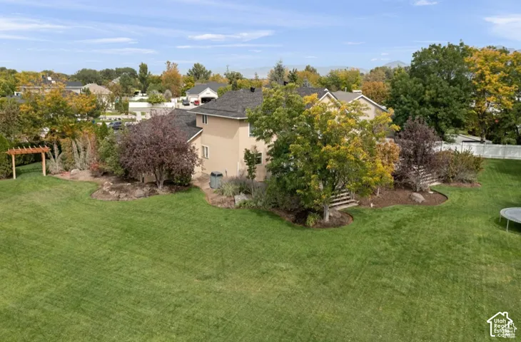 Spacious backyard featuring a lush lawn, mature trees, and a wooden pergola