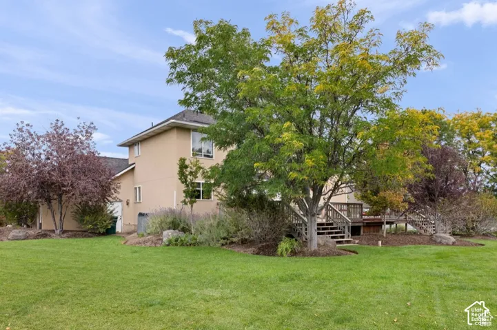 Spacious rear yard with a manicured lawn, mature trees, and a multi-level wood deck