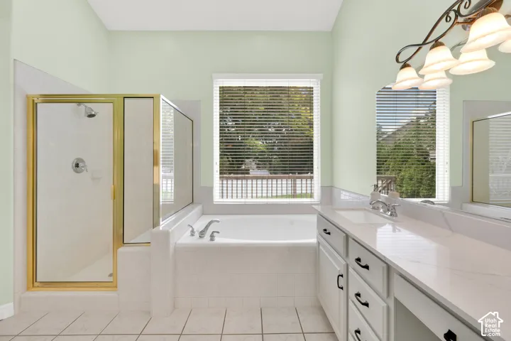 Spacious bathroom featuring a white soaking tub with deck-mounted faucet, a separate glass-enclosed shower with gold-tone framing, a double vanity with an integrated sink and white countertop, and tile flooring