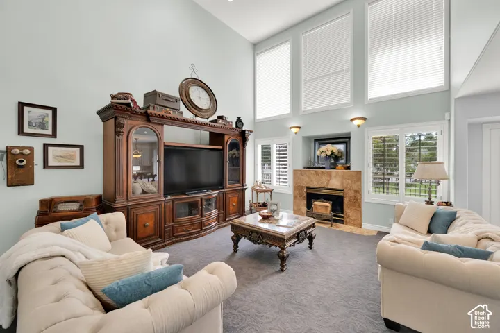 Living space featuring soaring vaulted ceilings, multiple tall windows with blinds, a fireplace with a stone surround, and plush carpet flooring