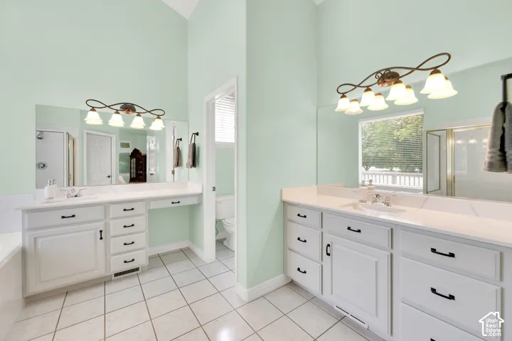Spacious bathroom featuring twin vanity areas with white cabinetry, light-toned countertops, and integrated sinks