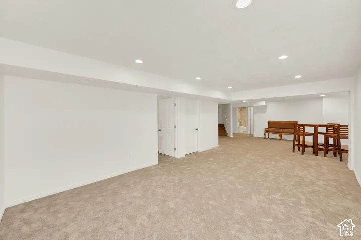 Spacious room featuring neutral carpeting, recessed lighting, white walls, and a visible doorway with a paneled door