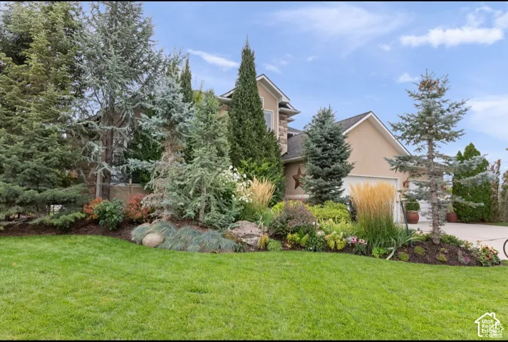 Stone and stucco exterior featuring an attached garage and a maturely landscaped front yard with a manicured lawn
