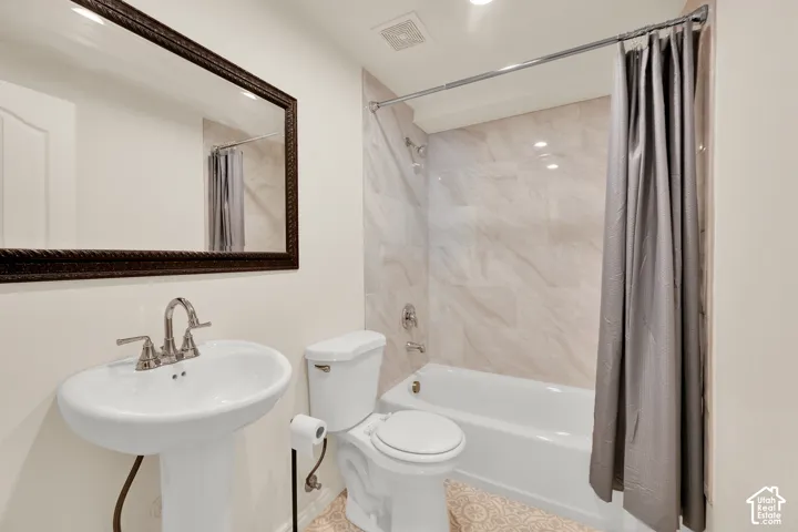 Bathroom featuring a pedestal sink with brushed nickel fixtures, a dark wood-framed mirror, and a bathtub with a tiled shower surround