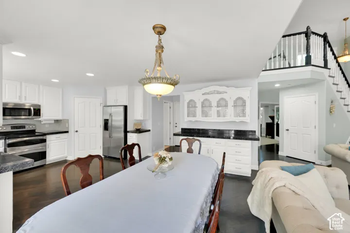 Open-concept living space featuring a dark wood-finish floor, white kitchen cabinetry with stainless steel appliances, a built-in display hutch, and a staircase with white and black banisters