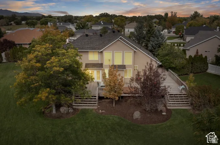 Rear exterior featuring a large wood-finish deck with multiple staircases, mature trees, and a spacious lawn