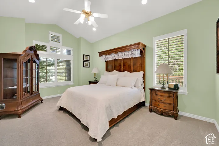 Vaulted ceiling bedroom featuring plush carpet flooring, a multi-tiered window system with plantation shutters, recessed lighting, and a ceiling fan