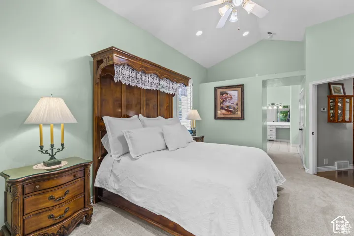 Vaulted ceiling bedroom featuring plush carpet flooring, a ceiling fan with light fixture, and a built-in vanity area with dual sinks visible
