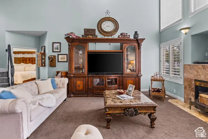 Living room featuring a built-in entertainment center, high ceilings, a fireplace with stone surround, large windows with plantation shutters, and an open doorway to another room