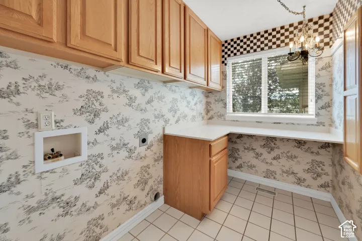 Functional utility room featuring extensive light wood cabinetry, a built-in countertop, a window with horizontal blinds, and a tiled floor