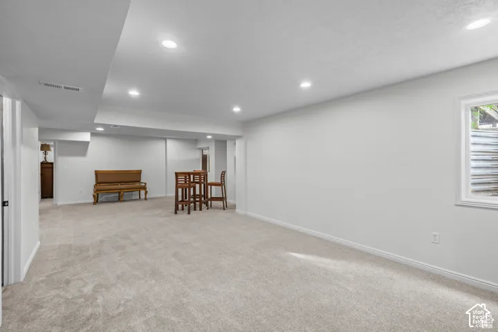 Spacious lower-level room featuring light gray carpeting, recessed ceiling lighting, a white painted window trim, and white baseboards