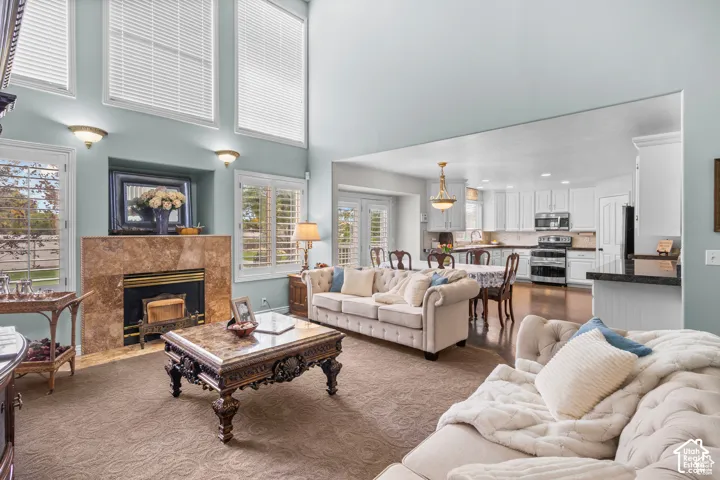 Living area featuring a floor-to-ceiling fireplace with stone surround, high ceilings, plantation shutters, and recessed wall sconces