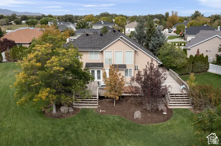 Rear exterior featuring a multi-level wooden deck with stairs, a spacious green lawn, and mature trees