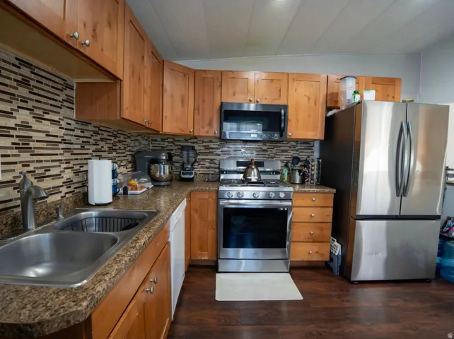Kitchen featuring wood-finish cabinetry, stainless steel appliances, a mosaic tile backsplash, and wood-finish flooring
