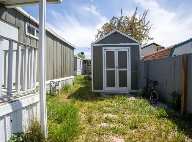 Detached storage shed with double doors, wood fencing, and a grassy area