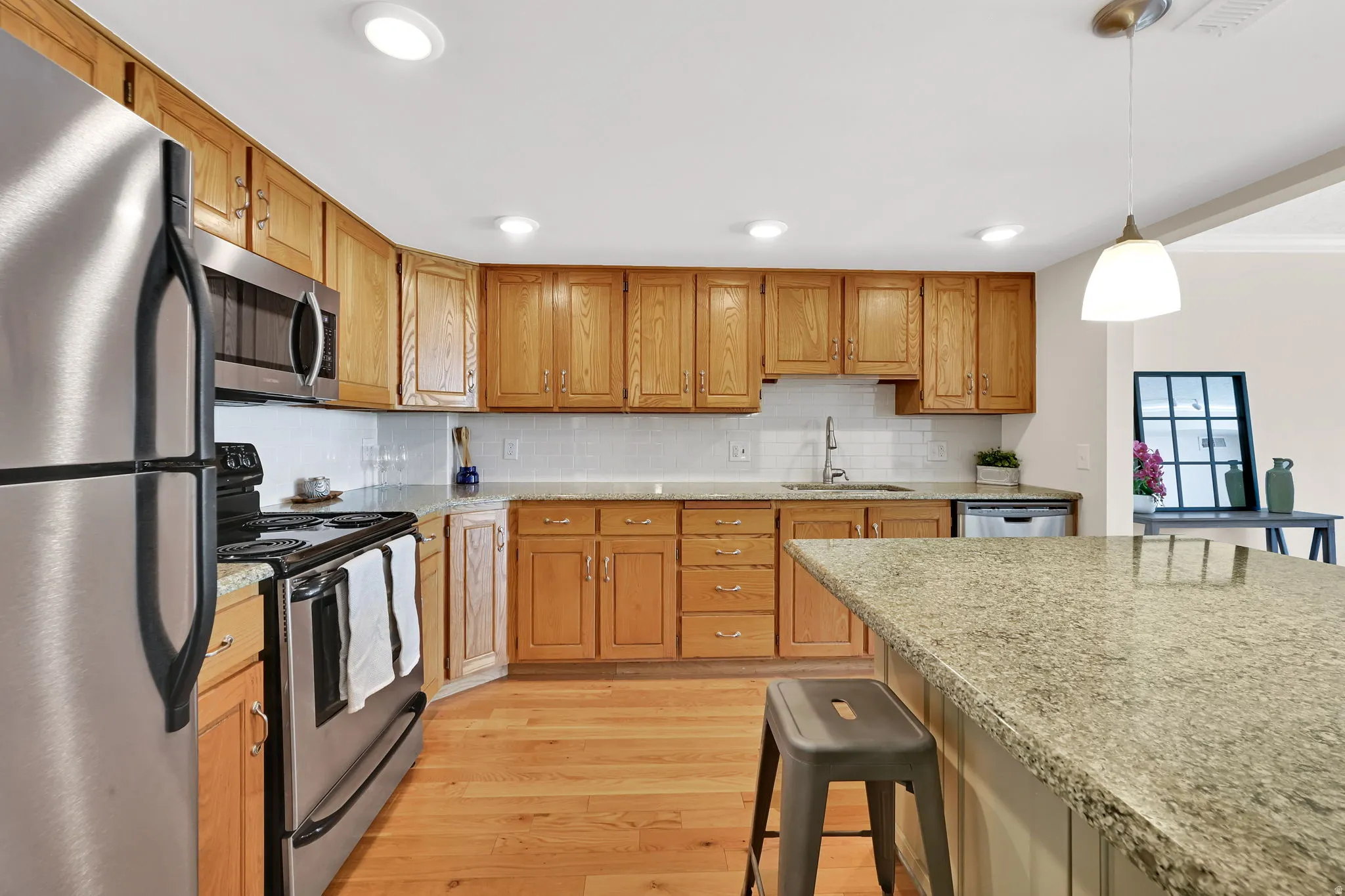 Kitchen featuring light wood cabinetry, granite countertops, stainless steel appliances, a subway tile backsplash, and wood-finish flooring