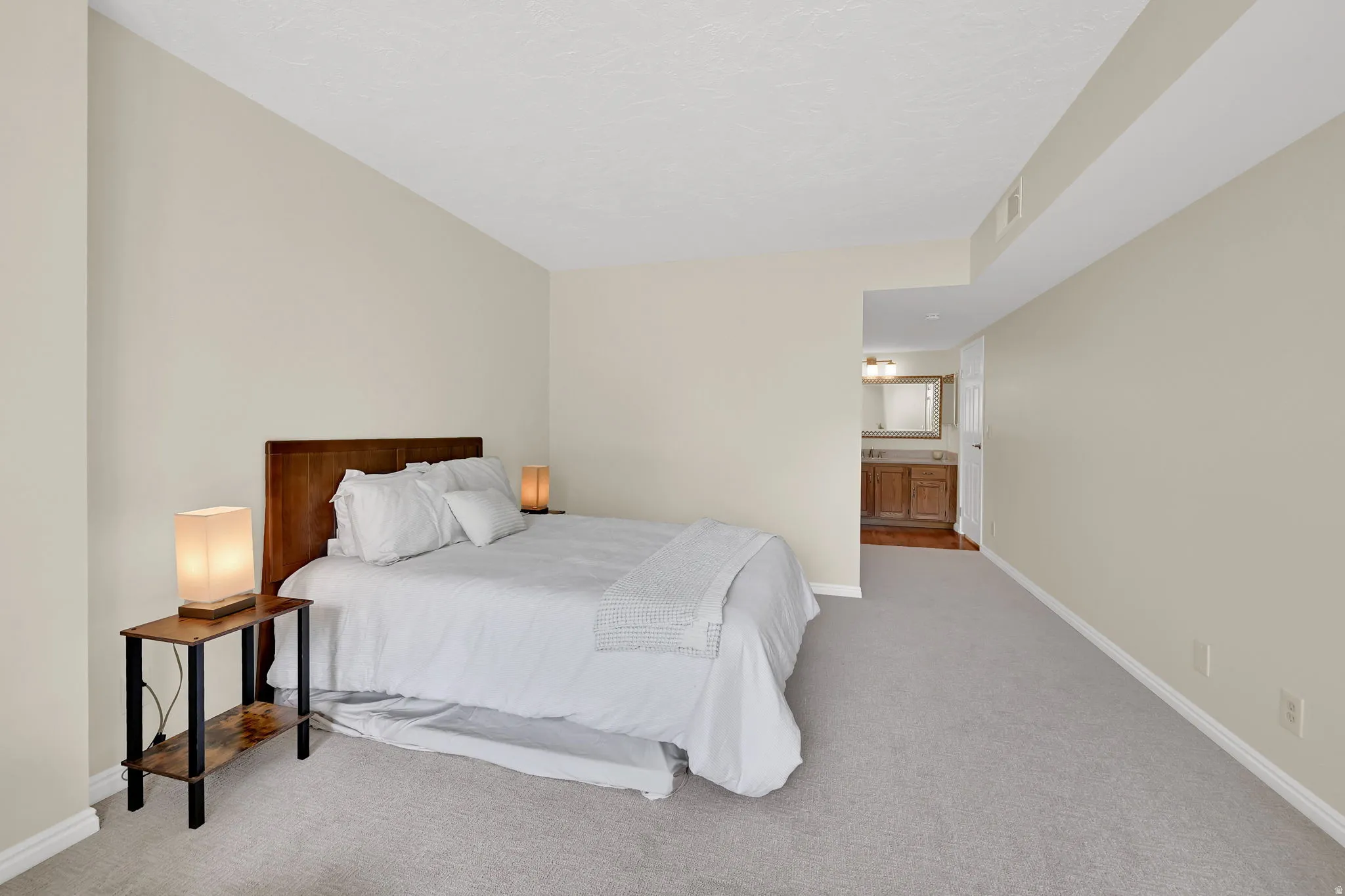 Spacious bedroom featuring light-colored carpet, neutral wall paint, and a wood headboard