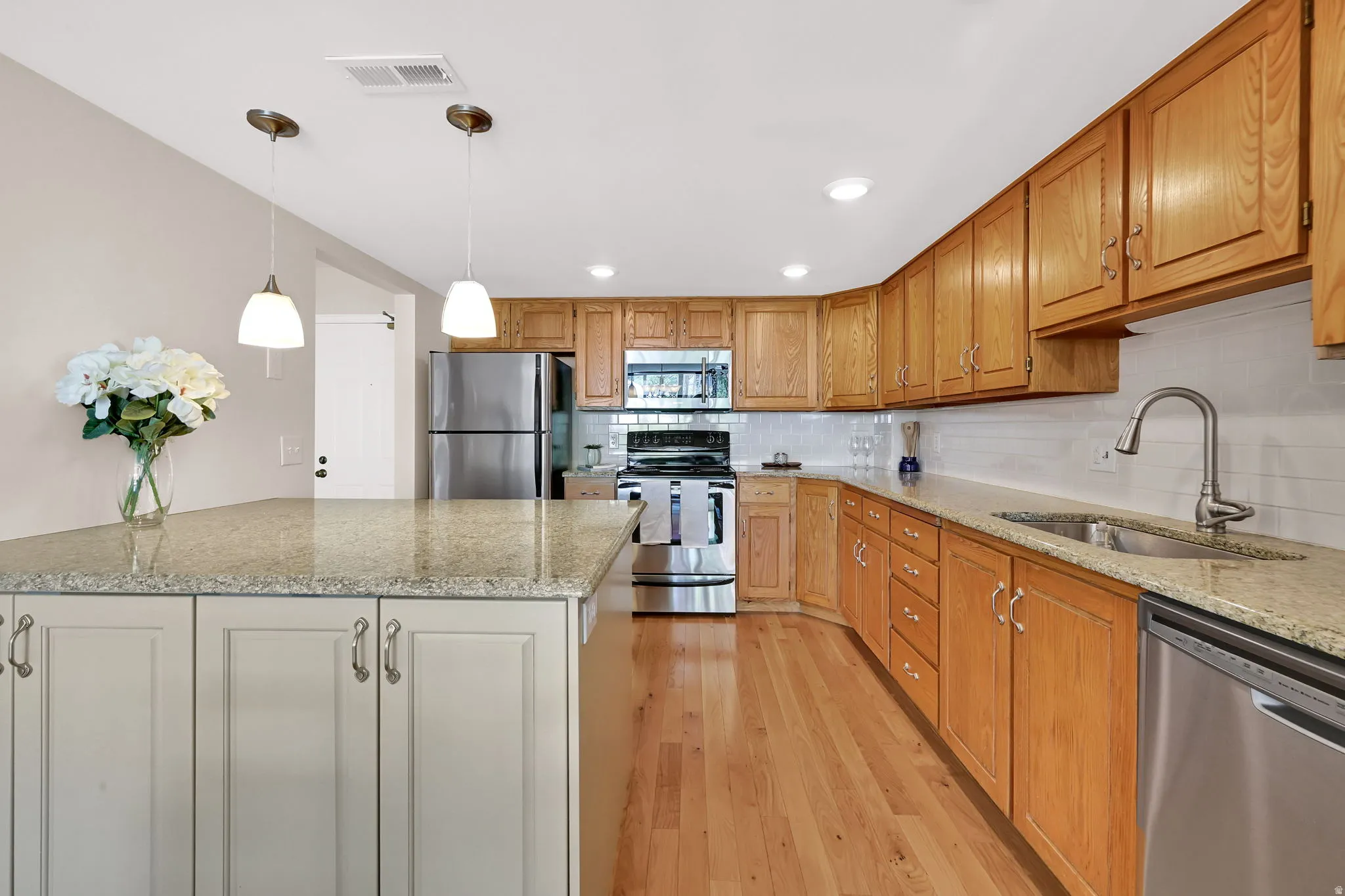 Kitchen featuring wood-finish flooring, stainless steel appliances, light wood cabinetry, and granite countertops