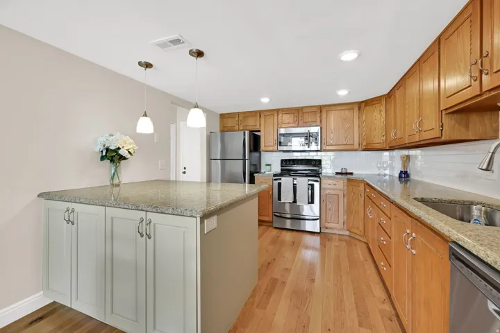 Kitchen featuring wood-finish flooring, light-colored granite countertops, and a white subway tile backsplash