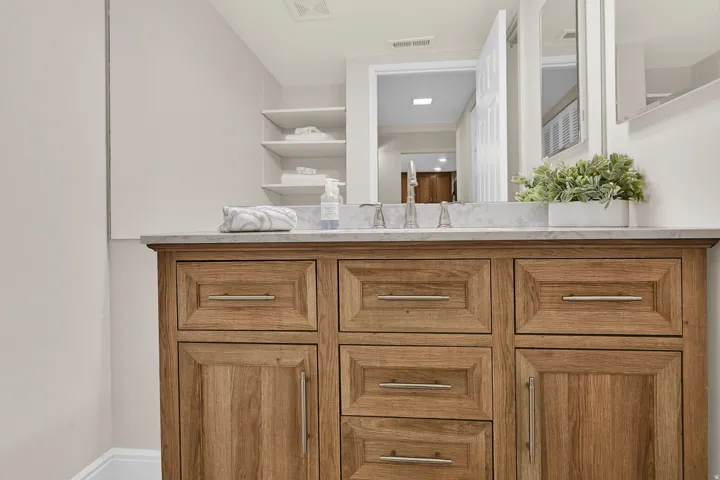 Wood-finish vanity with a light-toned countertop, brushed nickel hardware, and built-in shelving