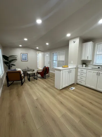 Open-concept living space featuring wood-finish flooring, recessed lighting, white kitchen cabinetry, and light-toned walls