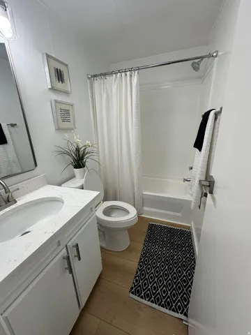 Full bathroom featuring a white vanity with a light-toned countertop, a built-in tub with a shower fixture, a toilet, and wood-finish flooring