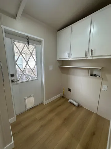 Utility room featuring wood-finish flooring, white cabinetry with silver hardware, and a white door with a diamond-patterned window insert