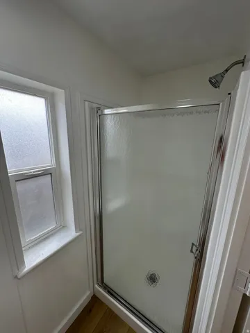 Shower enclosure featuring a sliding frosted glass door, chrome hardware, and a rainfall showerhead