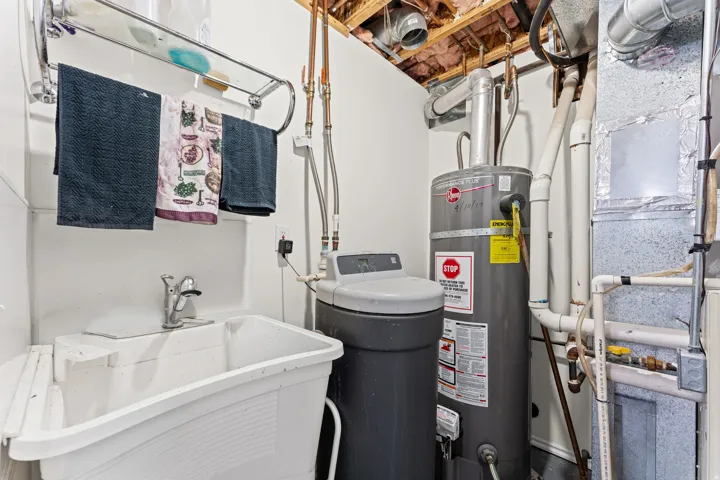 Utility area featuring a laundry sink with a wall-mounted faucet, a water heater, and a water softener system
