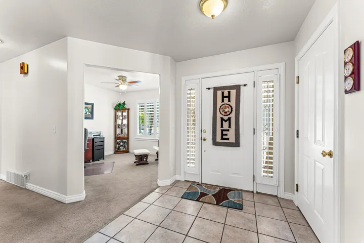 Entryway featuring a white paneled front door with sidelights, tiled flooring, and an adjacent carpeted room with a ceiling fan