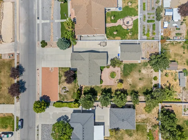 Aerial perspective highlighting a residential property with a detached garage, a concrete driveway, and a red paver patio