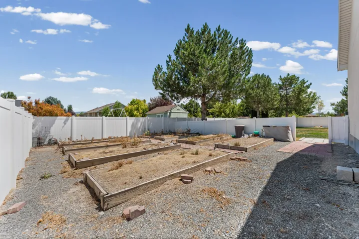 Spacious backyard featuring multiple raised garden beds, gravel ground cover, and a white vinyl privacy fence
